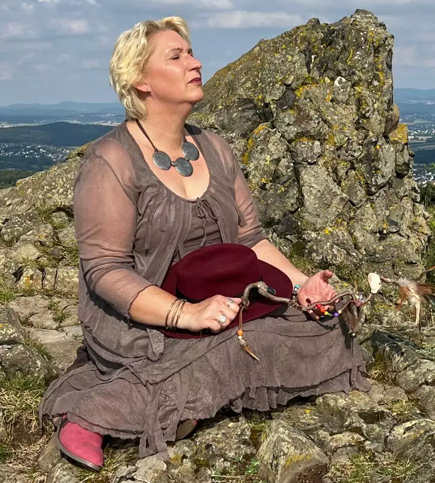 Josefine V.D. Kramer sitzt mit geschlossenen Augen auf einem Gebirgs-Gipfel. In der Hand hält sie ihren "Zauberstab" Josefine V.D. Kramer sitzt mit geschlossenen Augen auf einem Gebirgs-Gipfel. In der Hand hält sie ihren "Zauberstab"